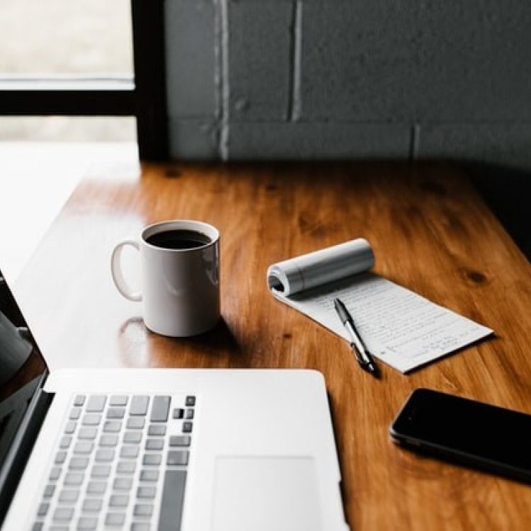 open laptop on a wood desk with coffee cup and notepad