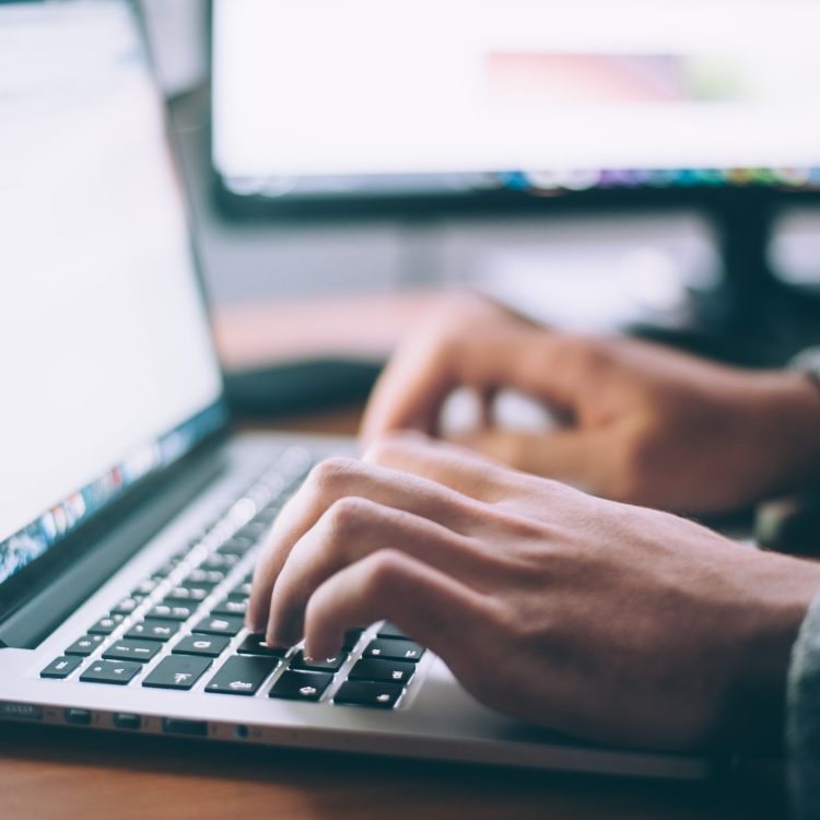 A close up photo of a person's hands typing on their laptop