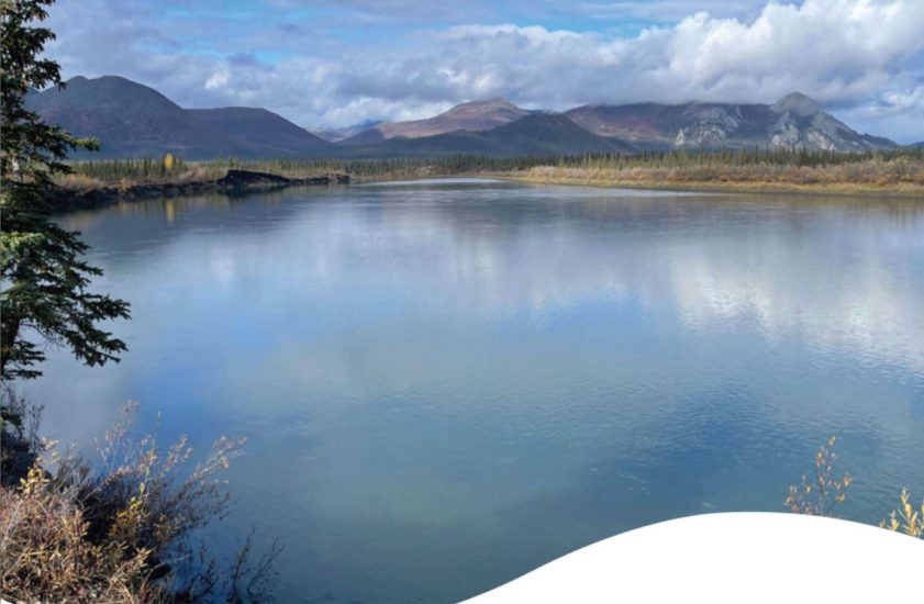 Glassy lake reflecting mountains in the distance with blue sky and clouds