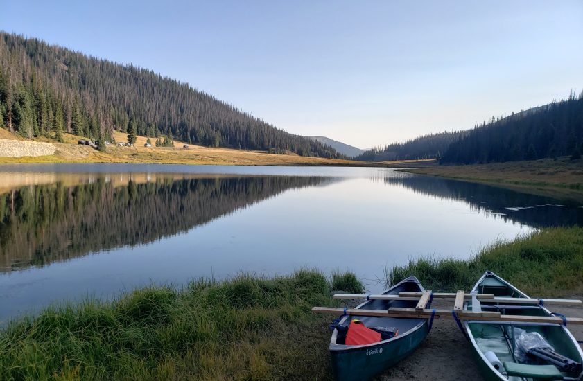 glassy lake reflecting mountains with two canoes in the foreground on the shore